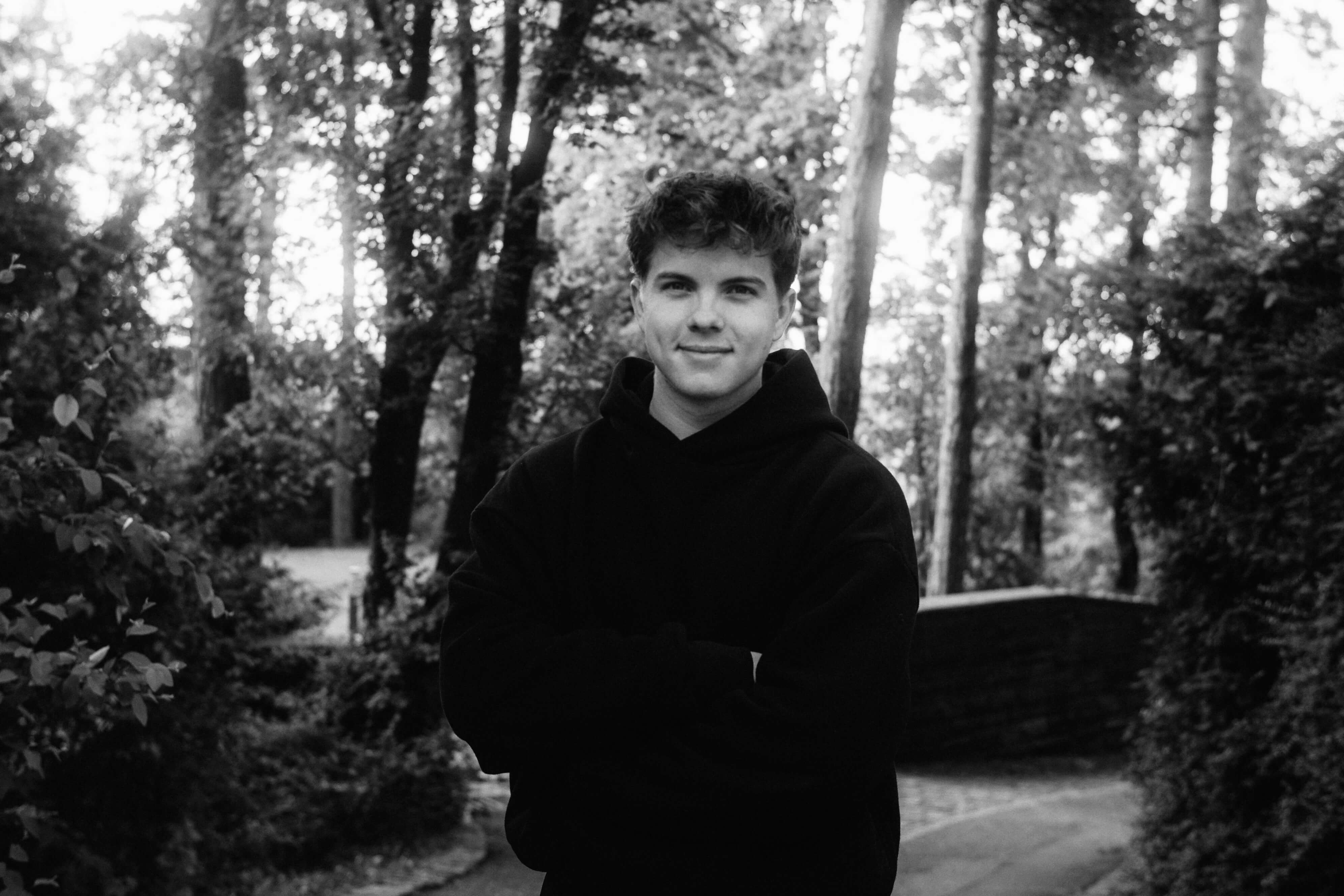 Black and white portrait of Paul Kühl, wearing a hoodie, standing in a park setting